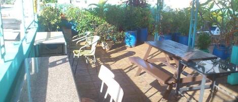 An outdoor patio area with a wooden table and chairs, surrounded by potted plants and a view of buildings in the background.