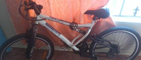 A white mountain bike with a black seat and handlebars, positioned indoors near a window with a curtain.