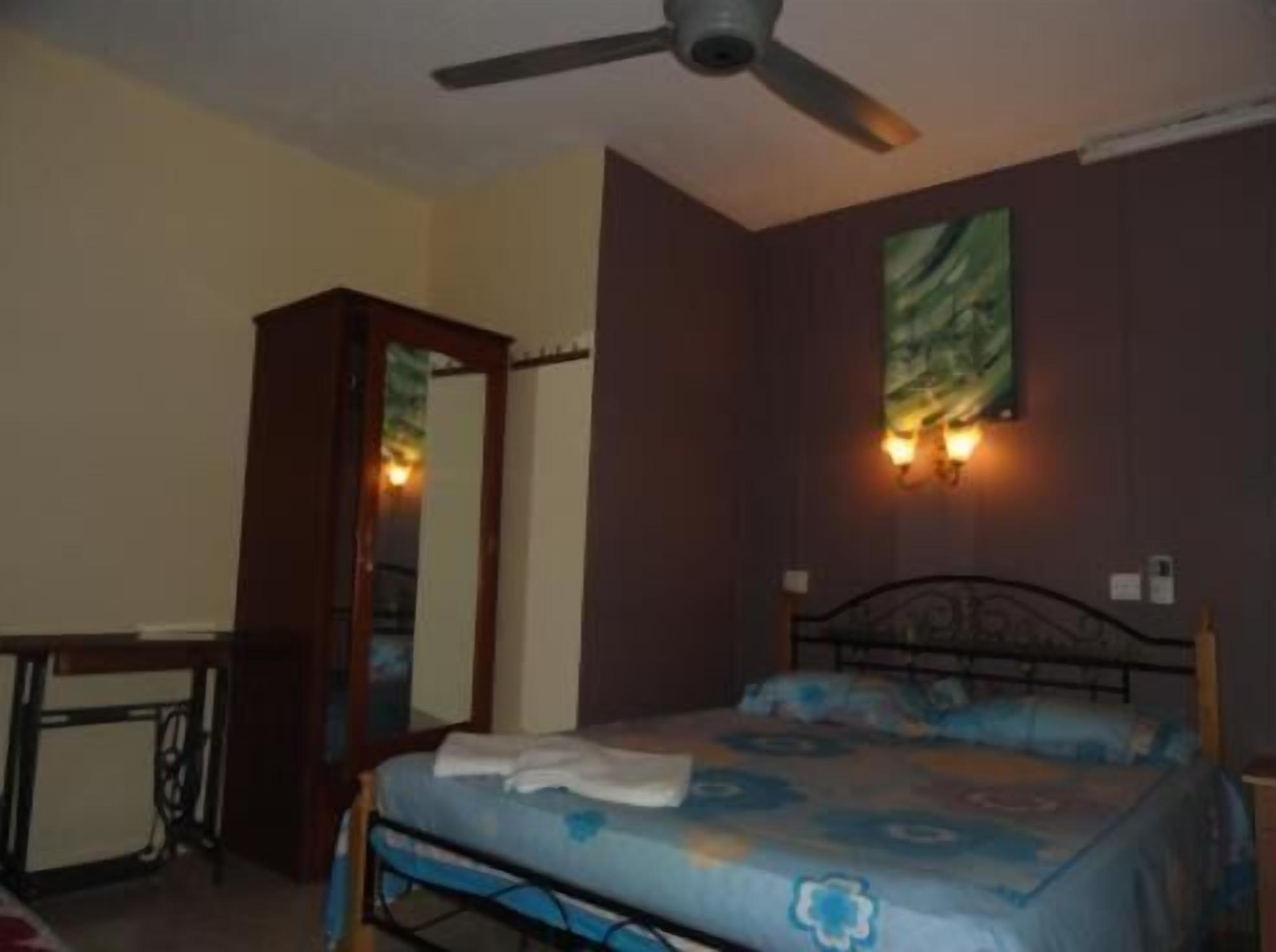A bedroom with a bed, a desk, a ceiling fan, and a wall-mounted light fixture.