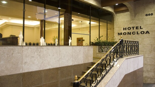 A hotel lobby with a marble staircase, a reception desk, and a sign reading "HOTEL MONCLOA".