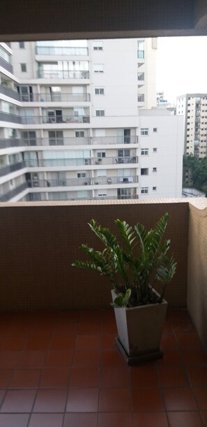 A balcony with a potted plant, a tiled floor, and a view of a multi-story building. - Hotel Moncloa (São Paulo)