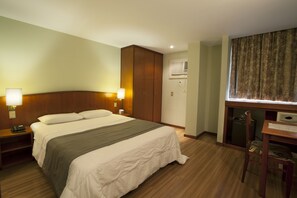 A hotel room with a bed, bedside lamps, a wardrobe, a desk with a chair, and a window with curtains. - Hotel Moncloa (São Paulo)