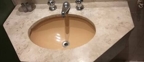 Un baño con un lavamanos color beige, dos grifos y un espejo.