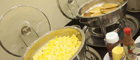A buffet setup with scrambled eggs, pancakes, and condiments like ketchup and mustard.