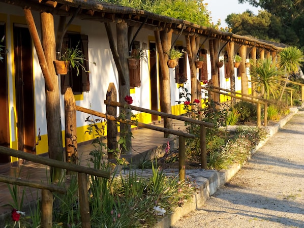 A rustic building with wooden beams and a yellow and white facade, featuring potted plants and a gravel pathway.