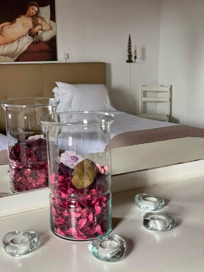 A bedroom with a bed, a nightstand, and two glass vases with pink flowers and a brown leaf.
