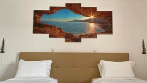 A hotel room with two beds, a wooden nightstand with a phone, and a large painting of a coastal sunset. - A Coutada Hotel Rural (Peniche)