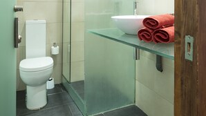 A modern bathroom with a glass shower enclosure, a white toilet, and a glass sink with a towel. - Vidre Home - Plaza Real (Barcelona)