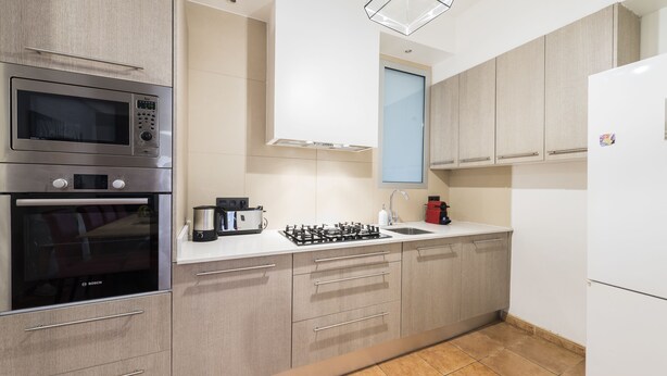 A modern kitchen with stainless steel appliances, wooden cabinets, and a tiled floor. - Vidre Home - Plaza Real (Barcelona)