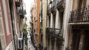 A narrow urban street with multi-story buildings, balconies, and pedestrians. - Vidre Home - Plaza Real (Barcelona)