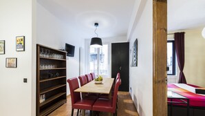 A dining area with a wooden table and red chairs, a bookshelf with glassware, and a view of the city through a window. - Vidre Home - Plaza Real (Barcelona)