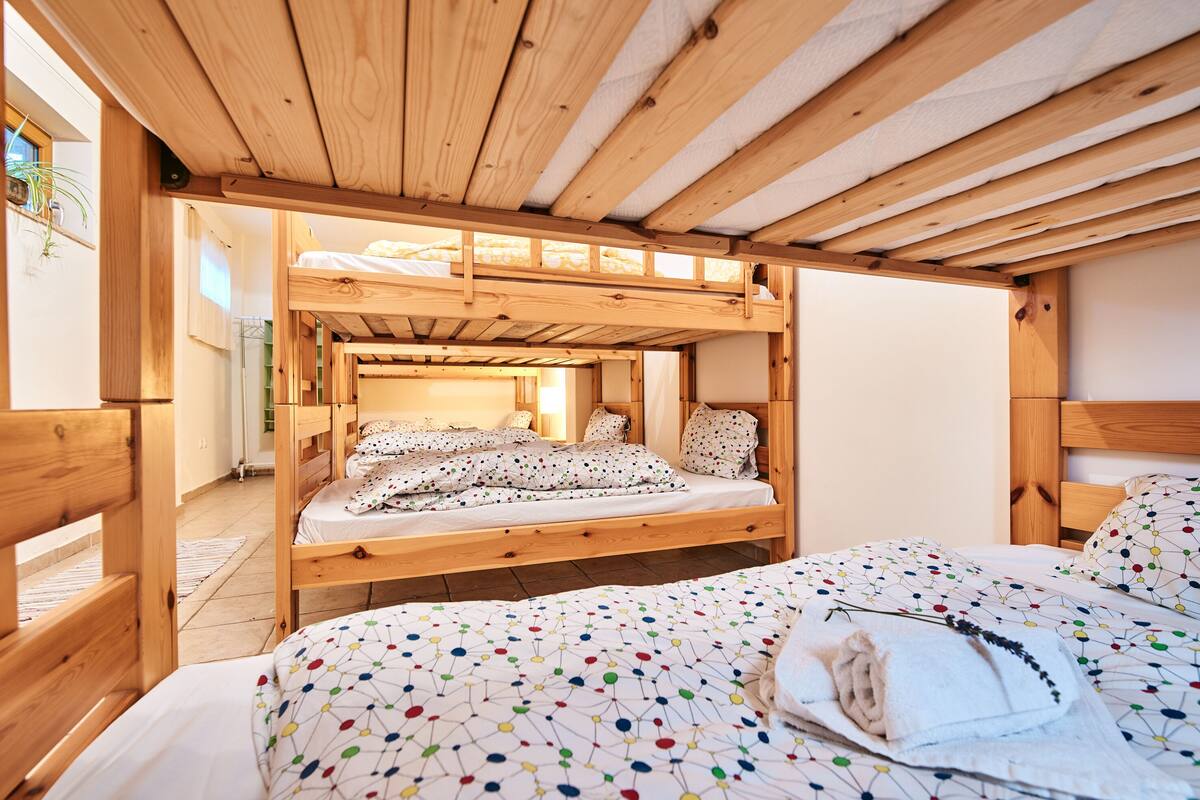 A wooden bunk bed room with a colorful polka dot bedspread, a wooden ceiling, and a view of a bathroom.