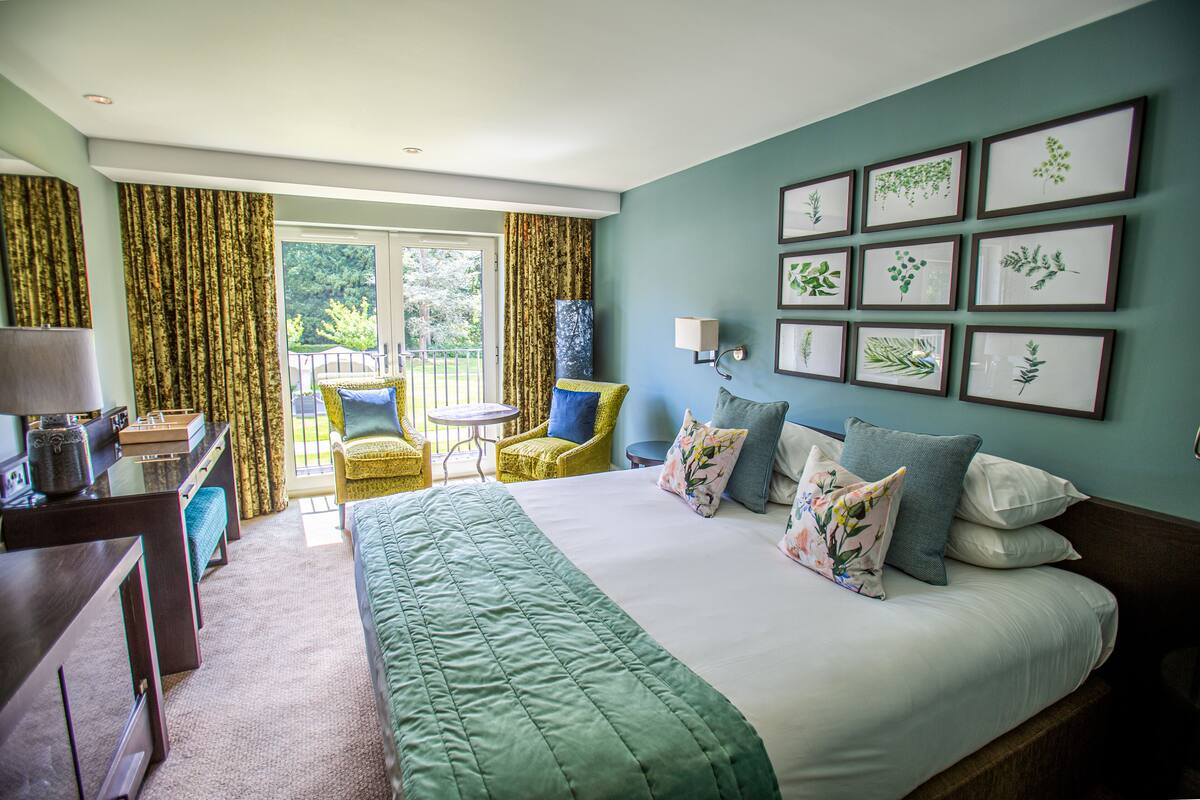 A hotel room with a large bed, a desk, a chair, and a balcony with curtains.
