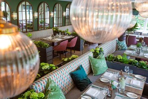 A restaurant with high-backed chairs, a long communal table, and a bench with cushions. - Hogarths Hotel (Solihull)