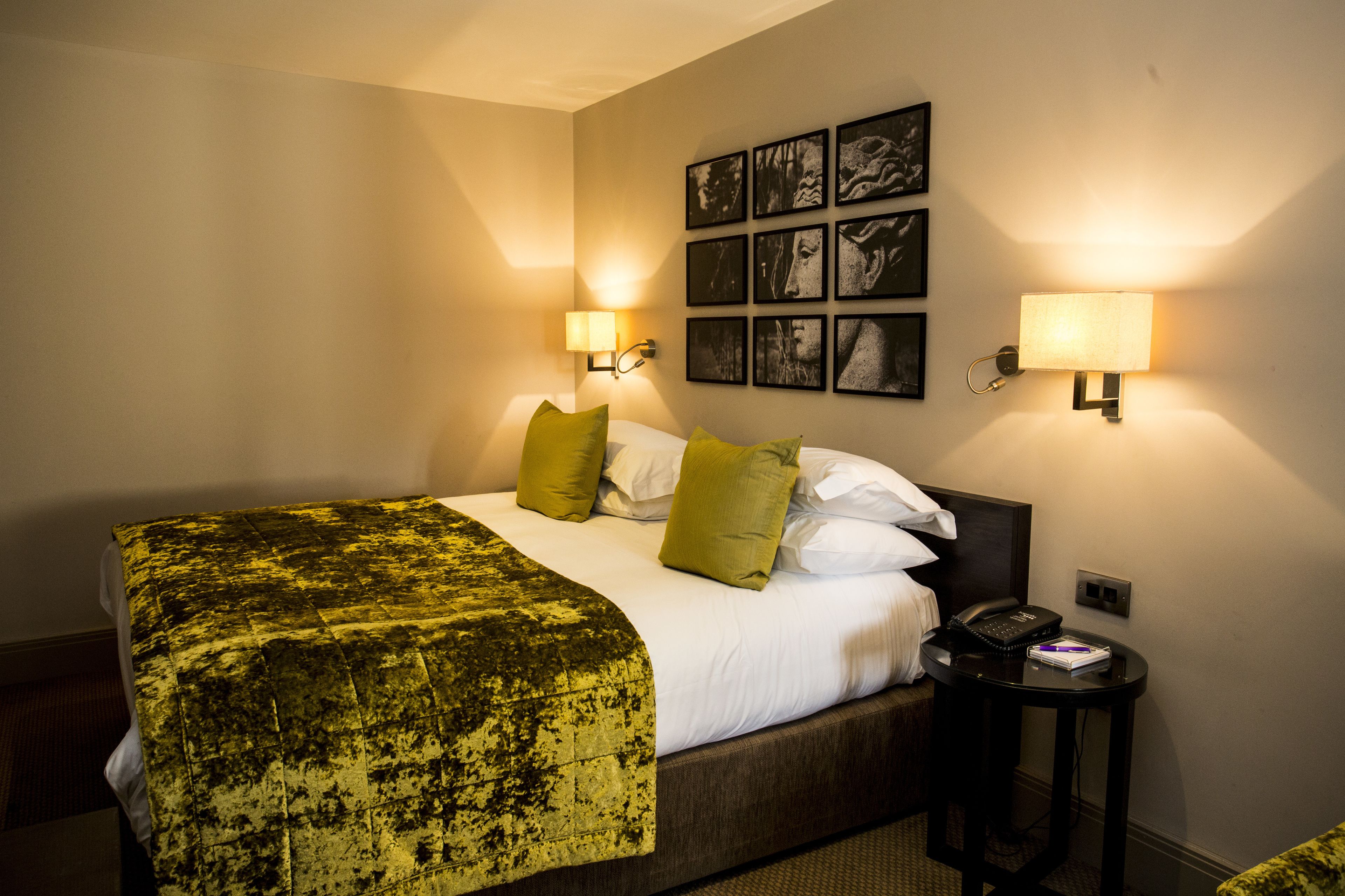 Une chambre d’hôtel comprenant un lit, deux lampes de chevet, un téléphone et un cadre photo fixé au mur.