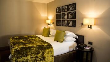 Une chambre d’hôtel comprenant un lit, deux lampes de chevet, un téléphone et un cadre photo fixé au mur.