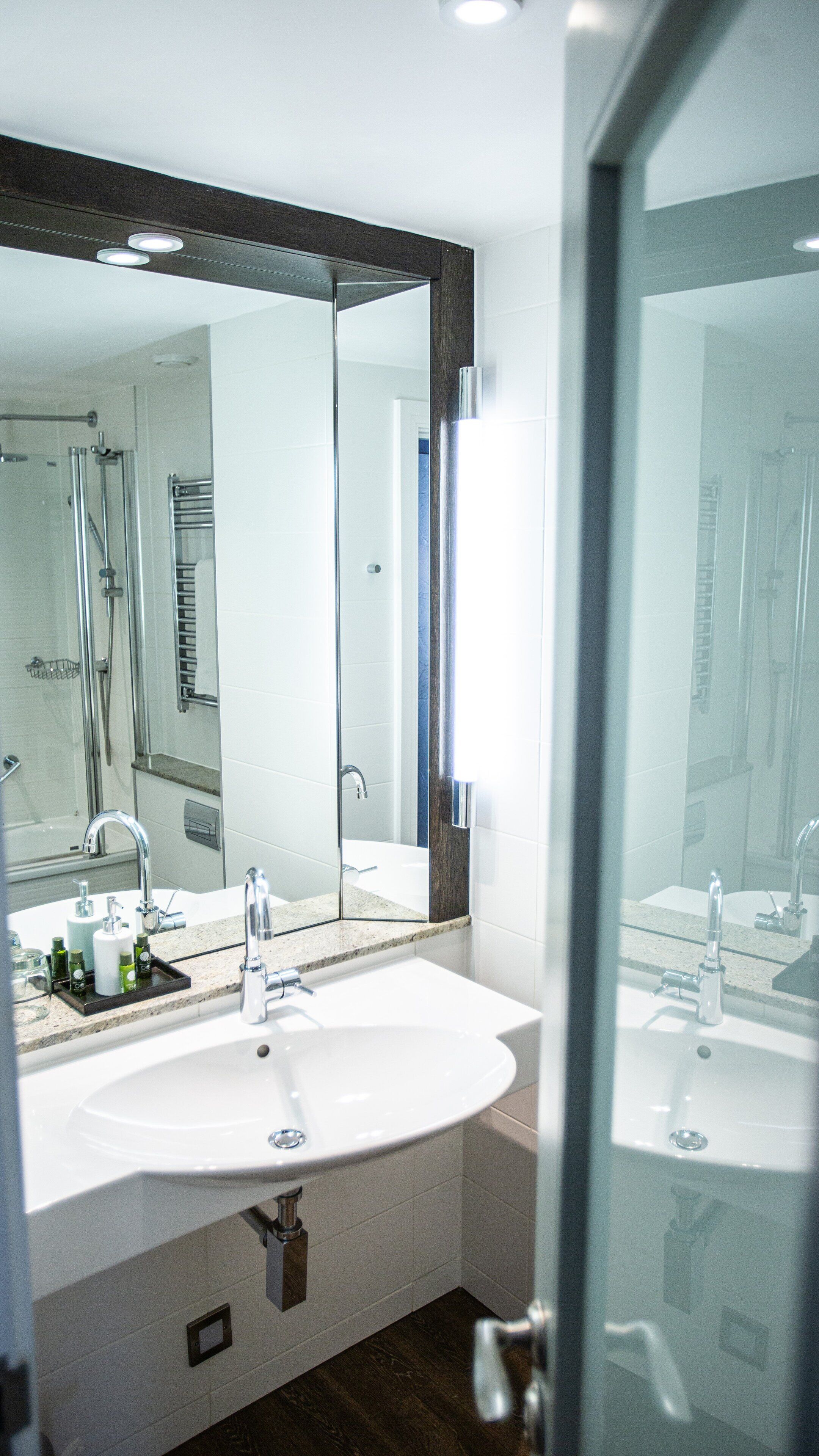 A modern bathroom with a large mirror, a sink, and a shower area.