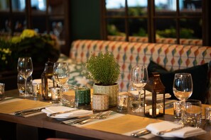 A dining table set with glassware, cutlery, and a potted plant, with a patterned sofa in the background. - Hogarths Hotel (Solihull)