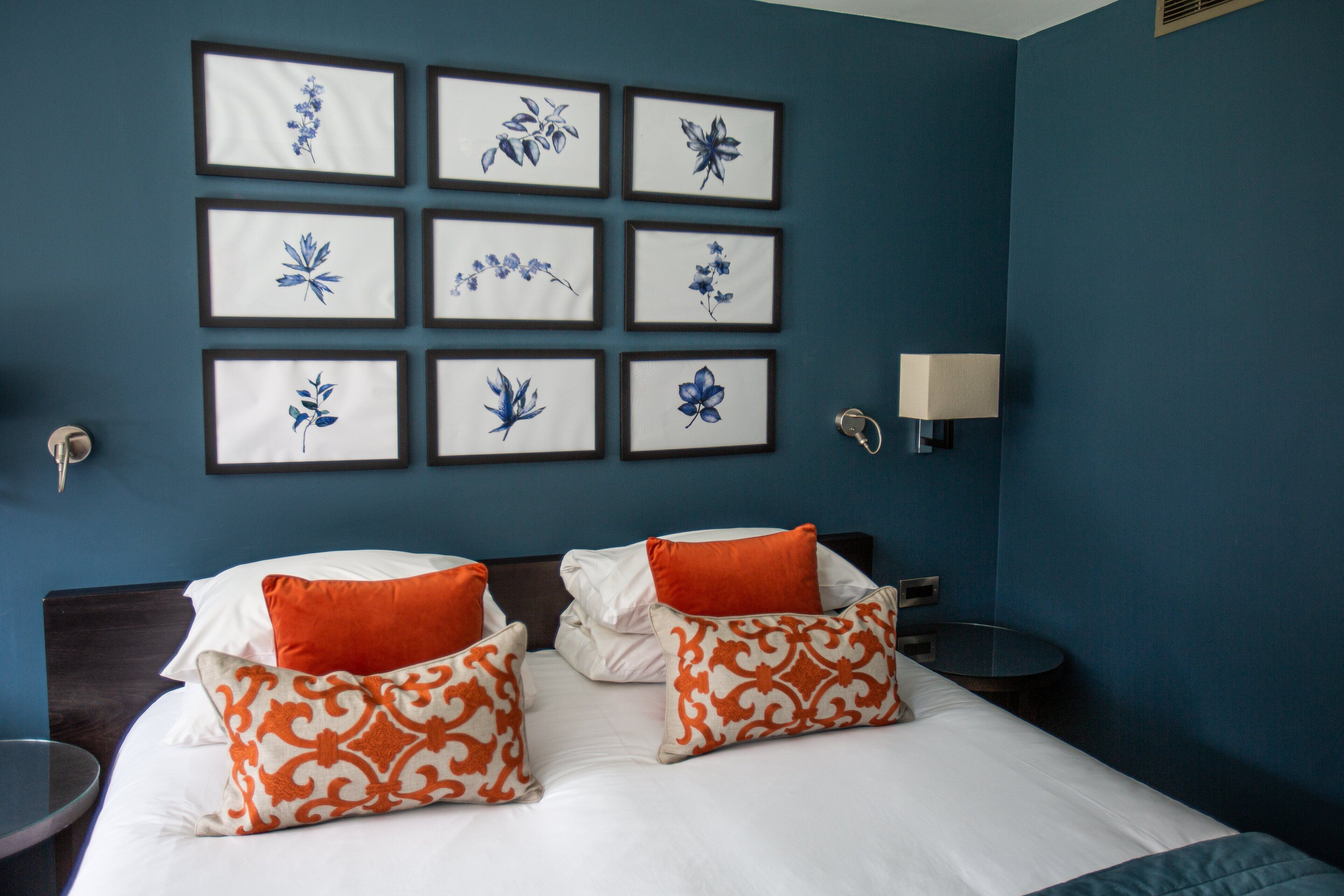 A hotel room with a large bed, two nightstands, a wall-mounted lamp, and framed floral artwork.