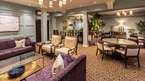 Eine geräumige Hotelhalle mit einem violetten Sofa, einem Glastisch und einem Essbereich mit rundem Tisch und Stühlen.