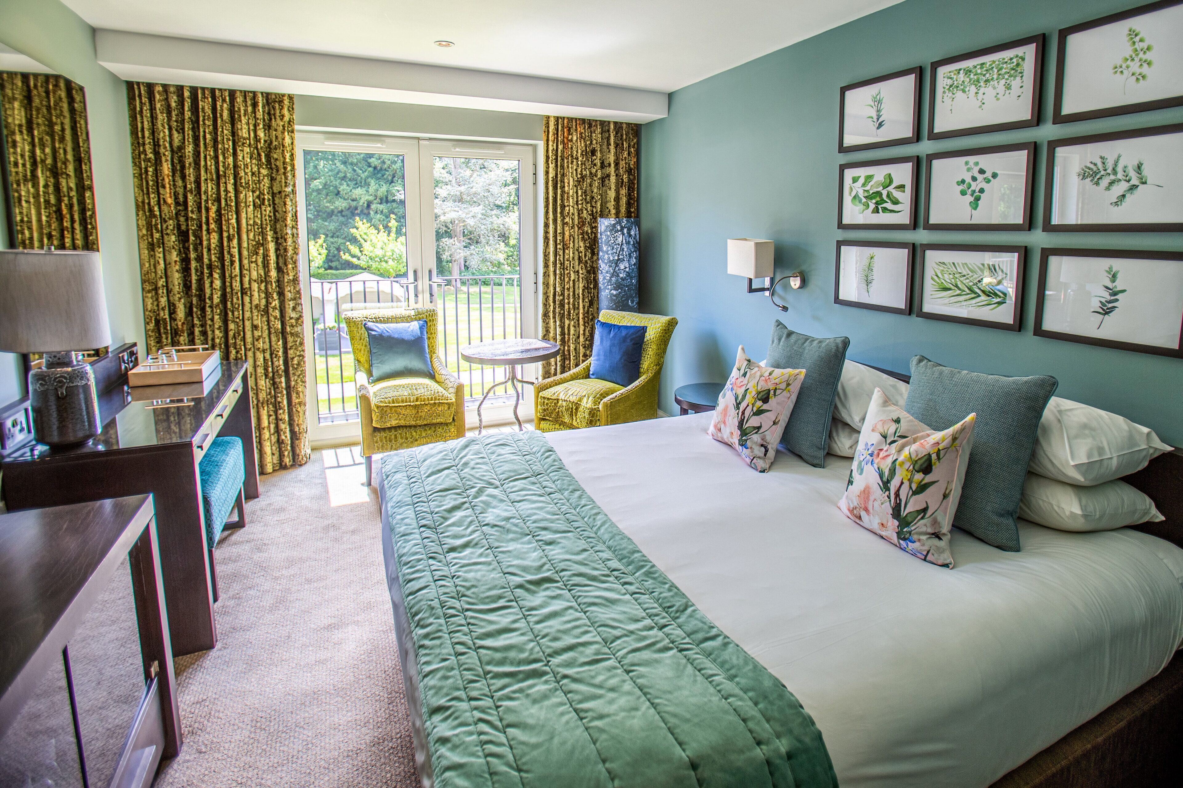 A hotel room with a bed, a desk, a chair, a small table, and a balcony with chairs.