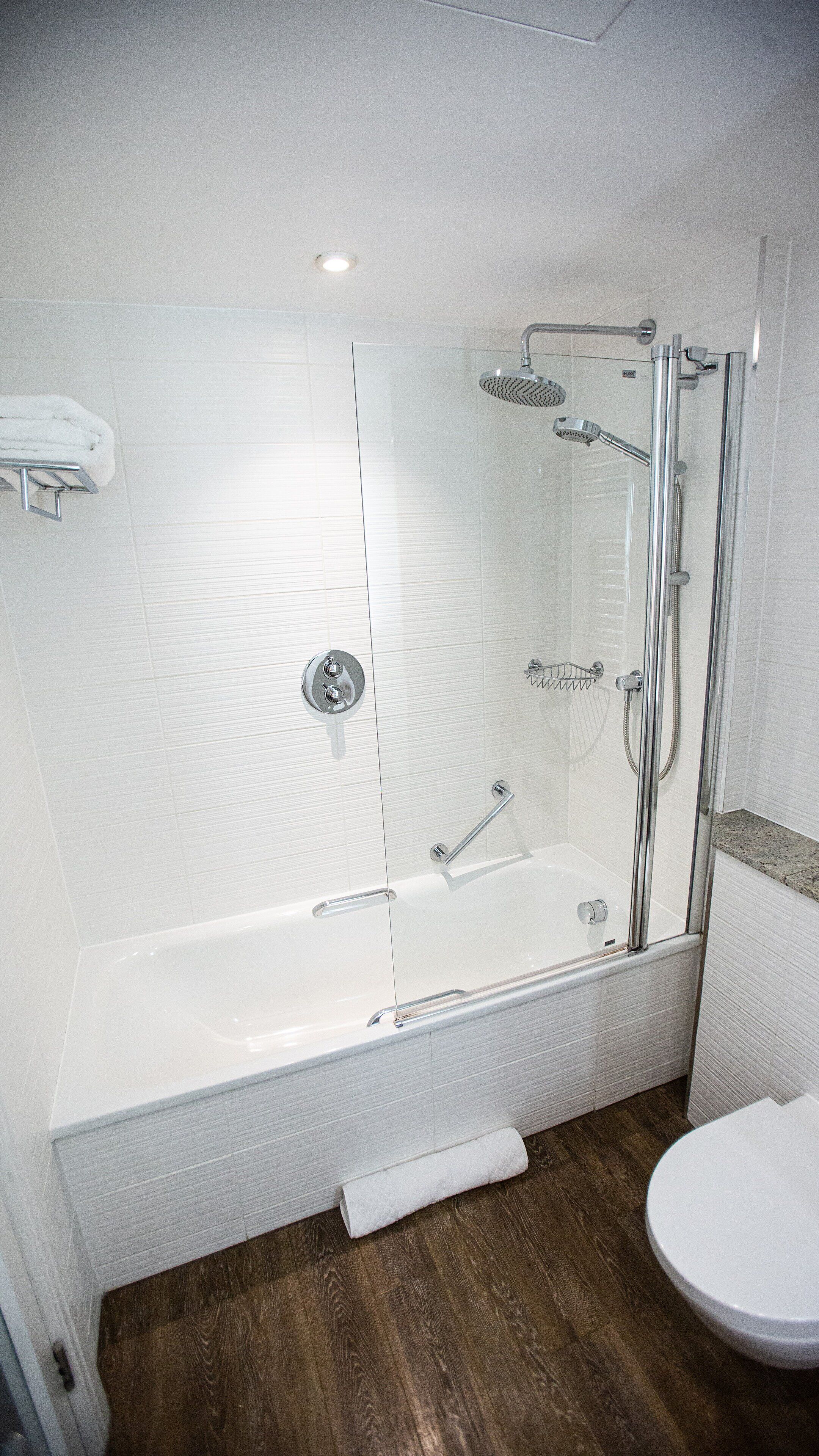 A modern bathroom with a glass-enclosed shower, a white bathtub, and a wooden floor.