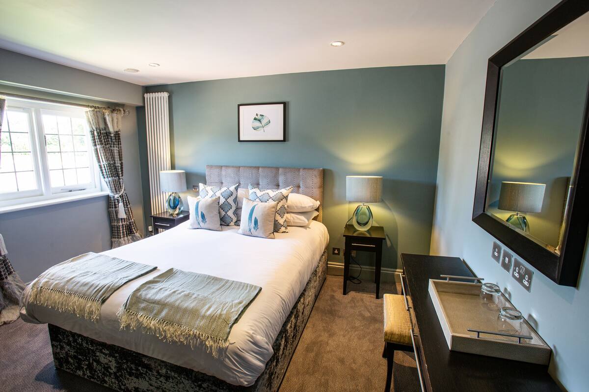 A hotel room with a large bed, bedside lamps, a small table with glasses, and a mirror on the wall.