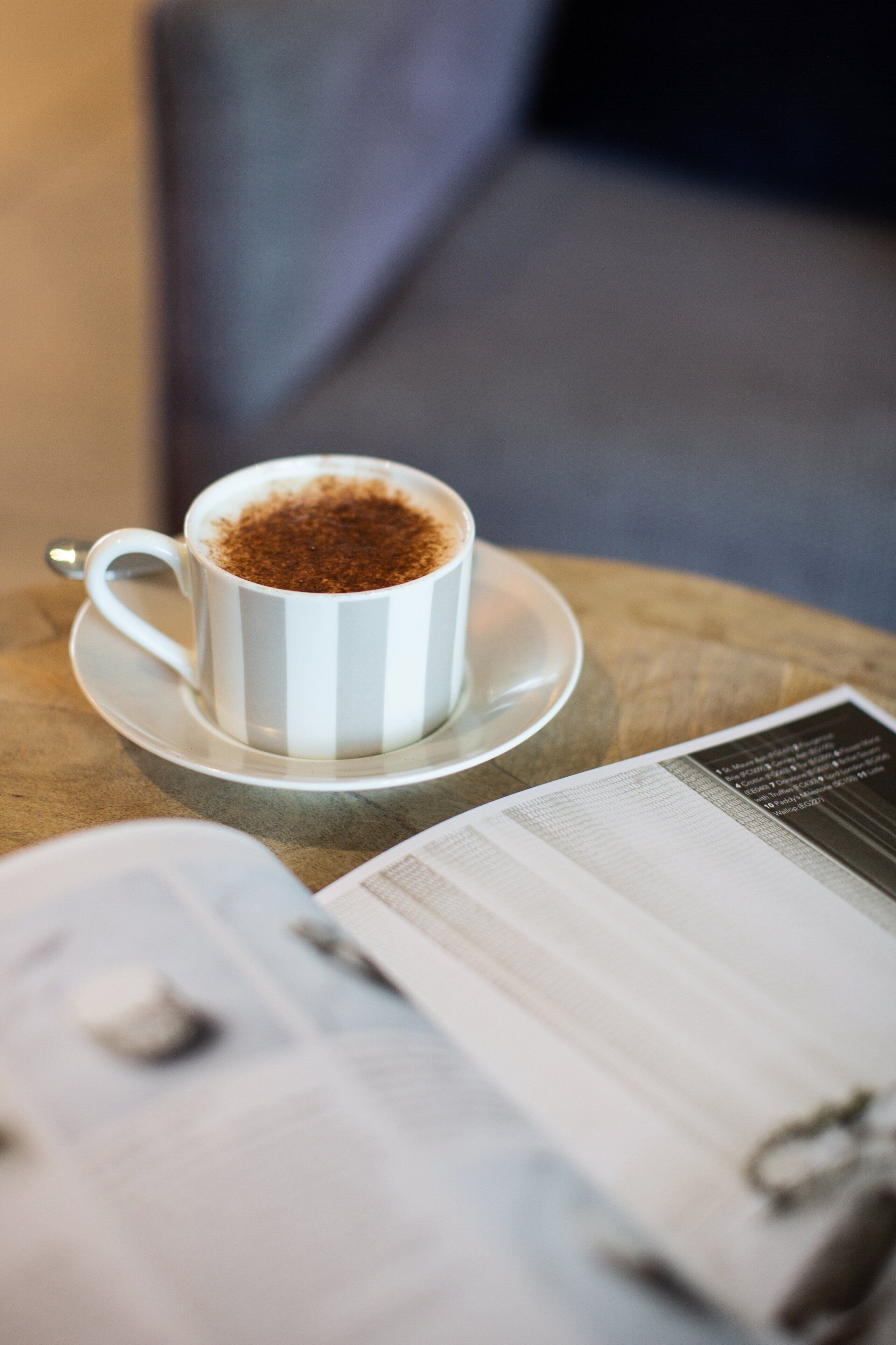 A white cup with a saucer on a table, next to an open magazine.