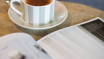 A white cup with a saucer on a table, next to an open magazine.