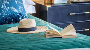 Una cama bien hecha con un edredón verde, un sombrero de paja y un libro abierto.