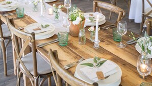 Ein Bankettraum mit runden Tischen, gedeckt für ein Essen, mit weißen Tischdecken, Holzsesseln und grünem Glas.