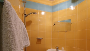 Un baño pequeño con azulejos amarillos y azules, un lavamanos blanco, un inodoro y una ducha con una toalla blanca colgada en la pared.