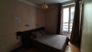 Un dormitorio con cama, lámpara colgante, ventana con cortinas y teléfono instalado en la pared.