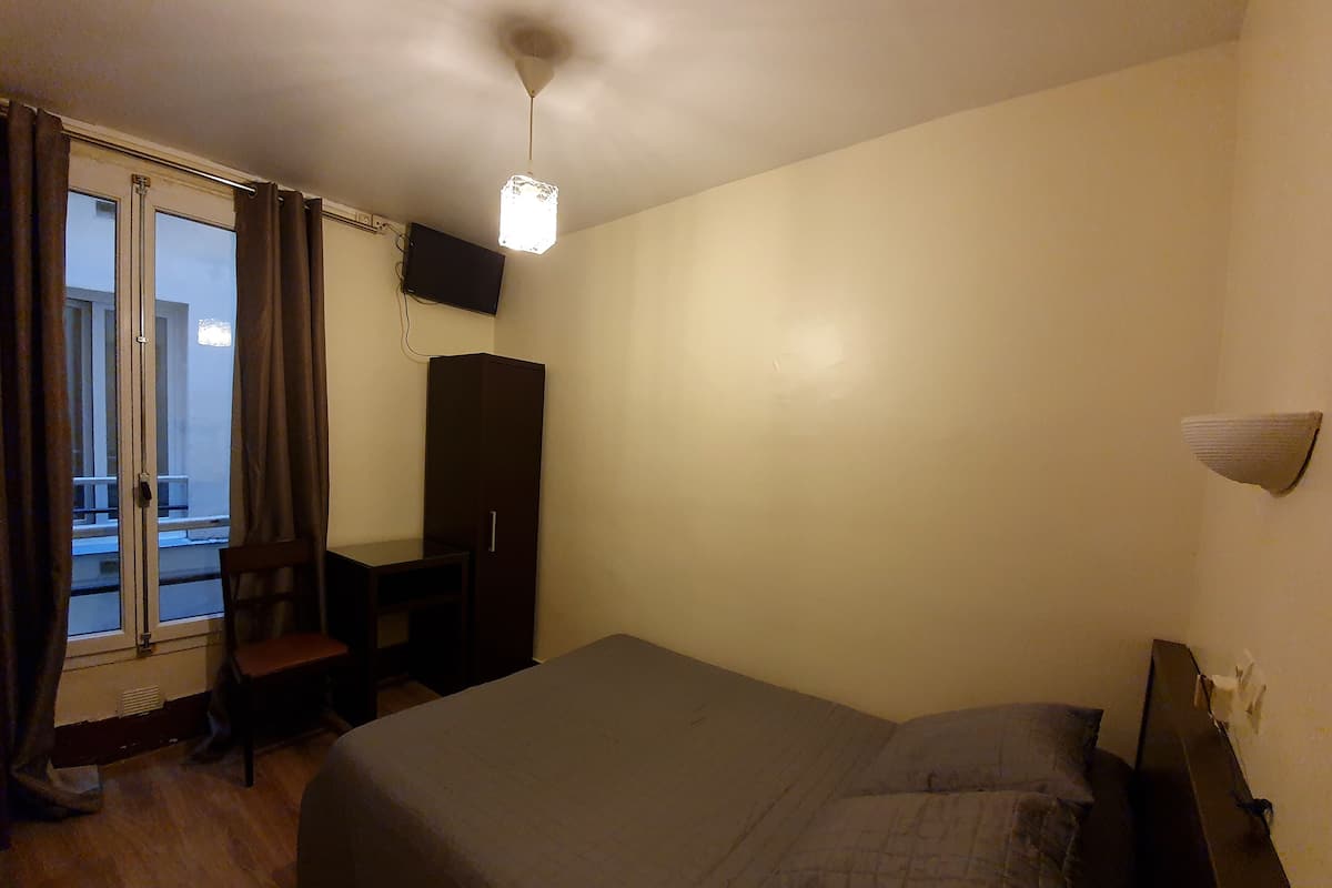 A bedroom with a bed, a desk, a wardrobe, and a window with curtains.