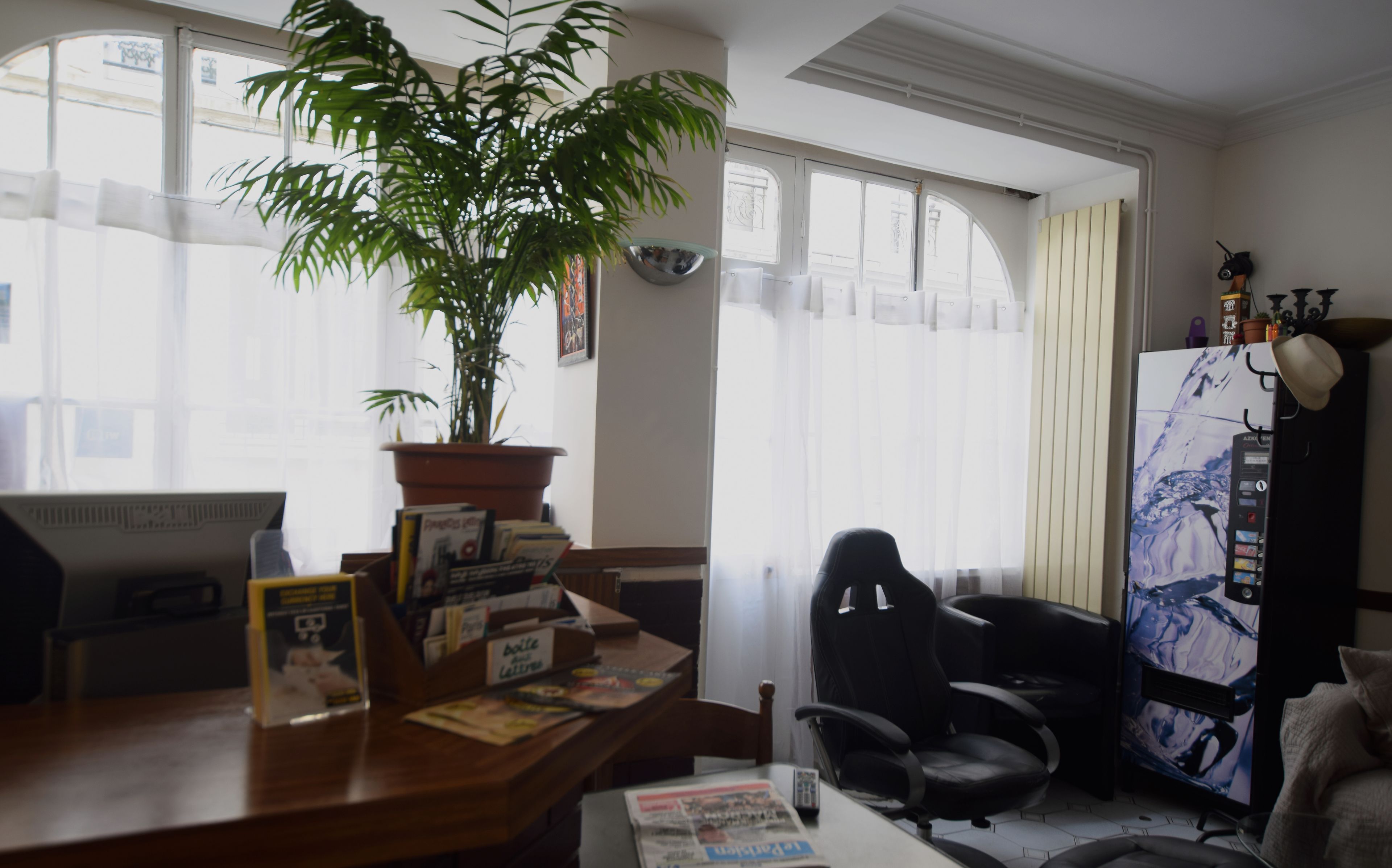 A room with a desk, a computer, a chair, a large window, and a refrigerator.