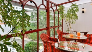 Un invernadero con estructura de metal rojo, paredes de cristal y una mesa con sillas.
