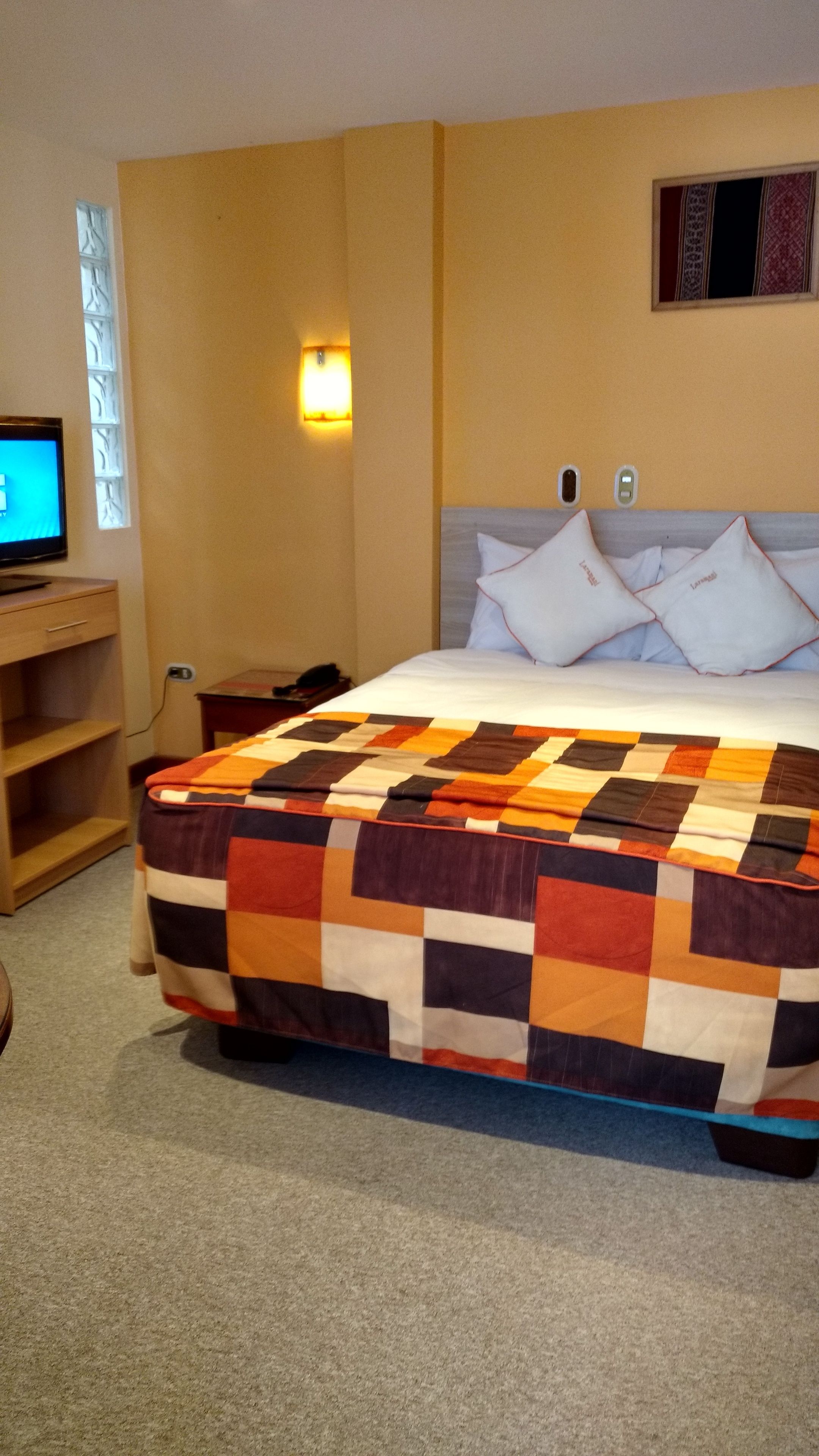 Une chambre d’hôtel avec un grand lit, un bureau avec un ordinateur, une fenêtre et une lampe fixée au mur.