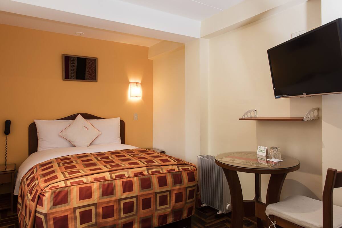 Habitación de hotel con cama, mesita de noche, silla, televisión y una pequeña mesa con un letrero.