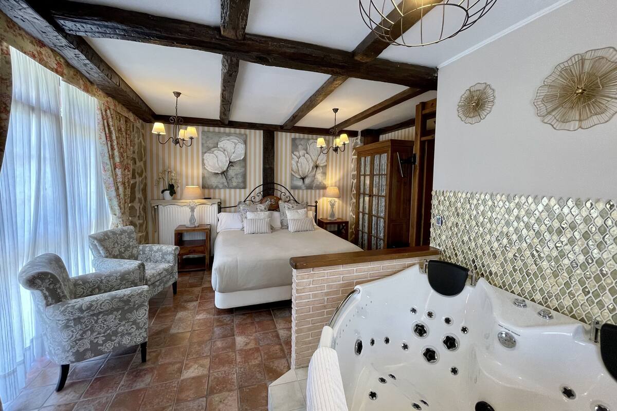 Ein Schlafzimmer mit einem großen Bett, einer Sitzecke mit Stühlen, einer Badewanne und einem Fenster mit Vorhängen.