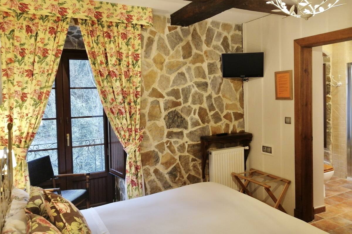 Ein Schlafzimmer mit einer Steinwand, einem Bett, einem hölzernen Stuhl, einem kleinen Tisch, einem Fernseher und einer Badezimmertür.