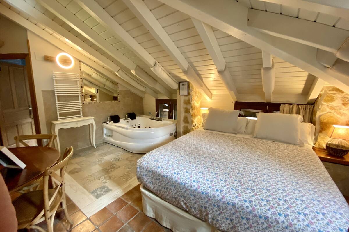 Ein Schlafzimmer mit einem großen Bett, einer Sitzecke mit einem Sessel, einer Badewanne und einem kleinen Tisch.