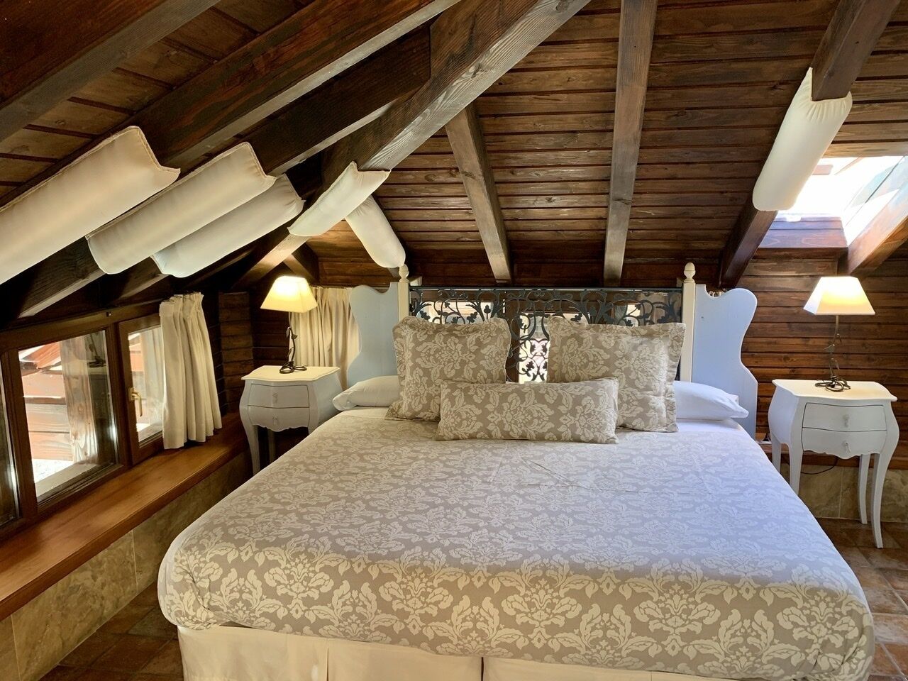 A bedroom with a large bed, two bedside tables, and a window with curtains.