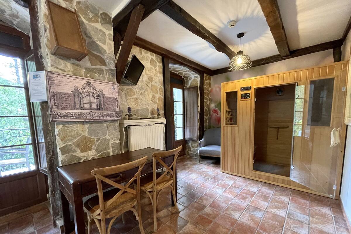 Ein rustikaler Raum mit Steinwänden, einem Holztisch mit Stühlen, einem Kamin und einem Holzschrank.
