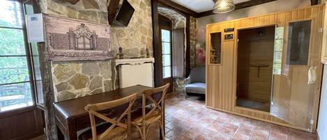 Una habitación rústica con paredes de piedra, una mesa de madera con sillas, chimenea y un armario de madera.