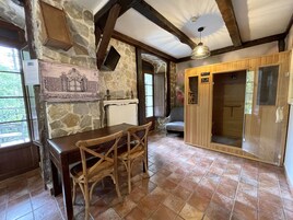 Una habitación rústica con paredes de piedra, una mesa de madera con sillas, chimenea y un armario de madera.