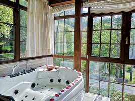 Una bañera de hidromasaje con pétalos de rosa, una ventana con vistas a la vegetación y un techo de madera.