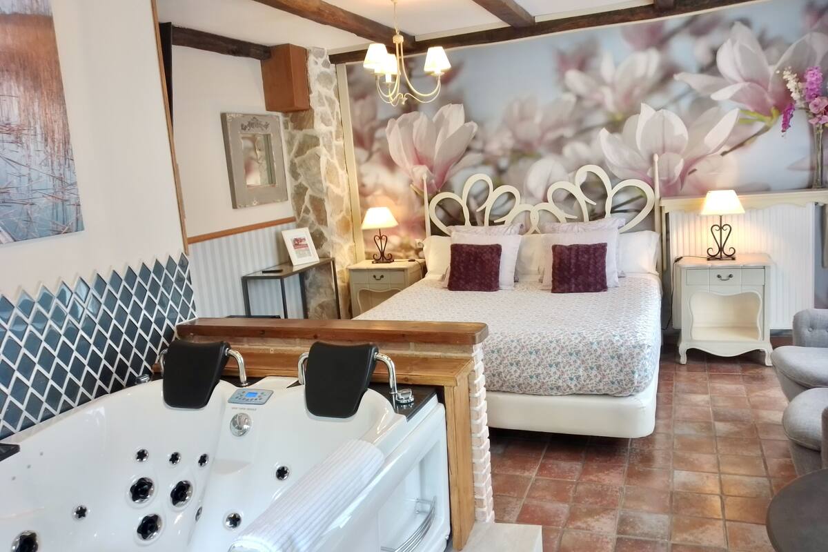 Ein Schlafzimmer mit einem großen Bett, einem hölzernen Kopfteil, einer weißen Badewanne und einer Wandmalerei mit Blumen.