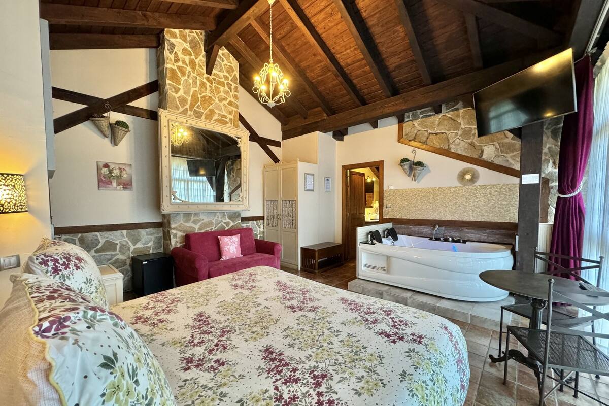 Ein Schlafzimmer mit einem großen Bett, einer Sitzecke mit einem roten Sofa, einer Wand aus Naturstein, einem großen Spiegel und einem Badezimmer mit einer Badewanne und einem Waschbecken.