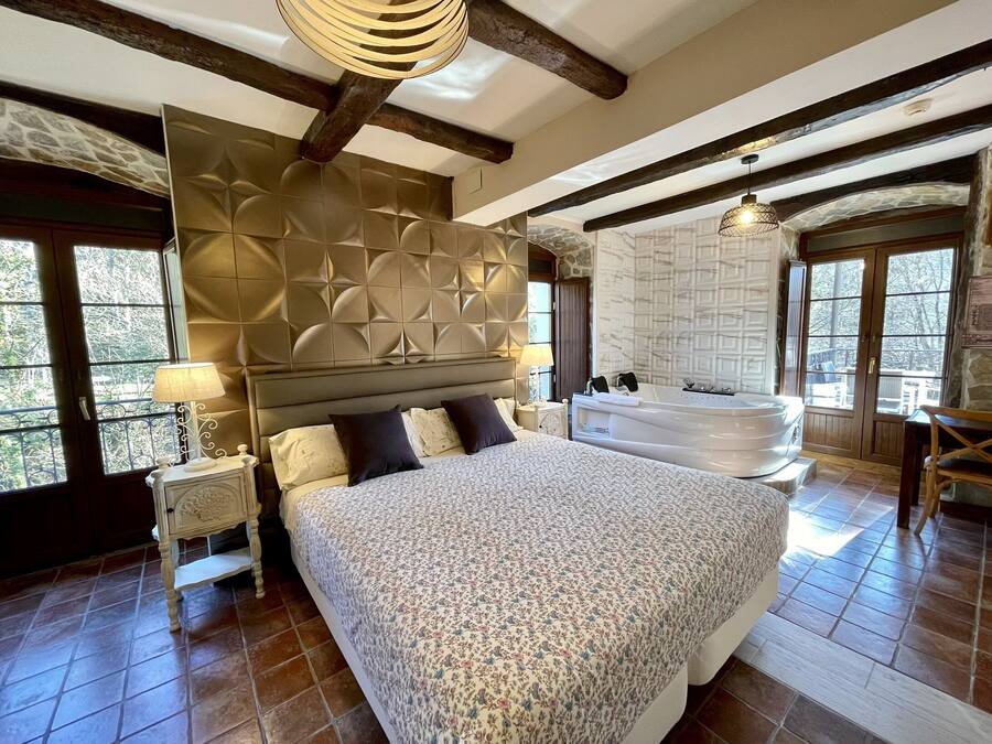 Un dormitorio amplio con una cama grande, una bañera integrada y una pared de piedra.