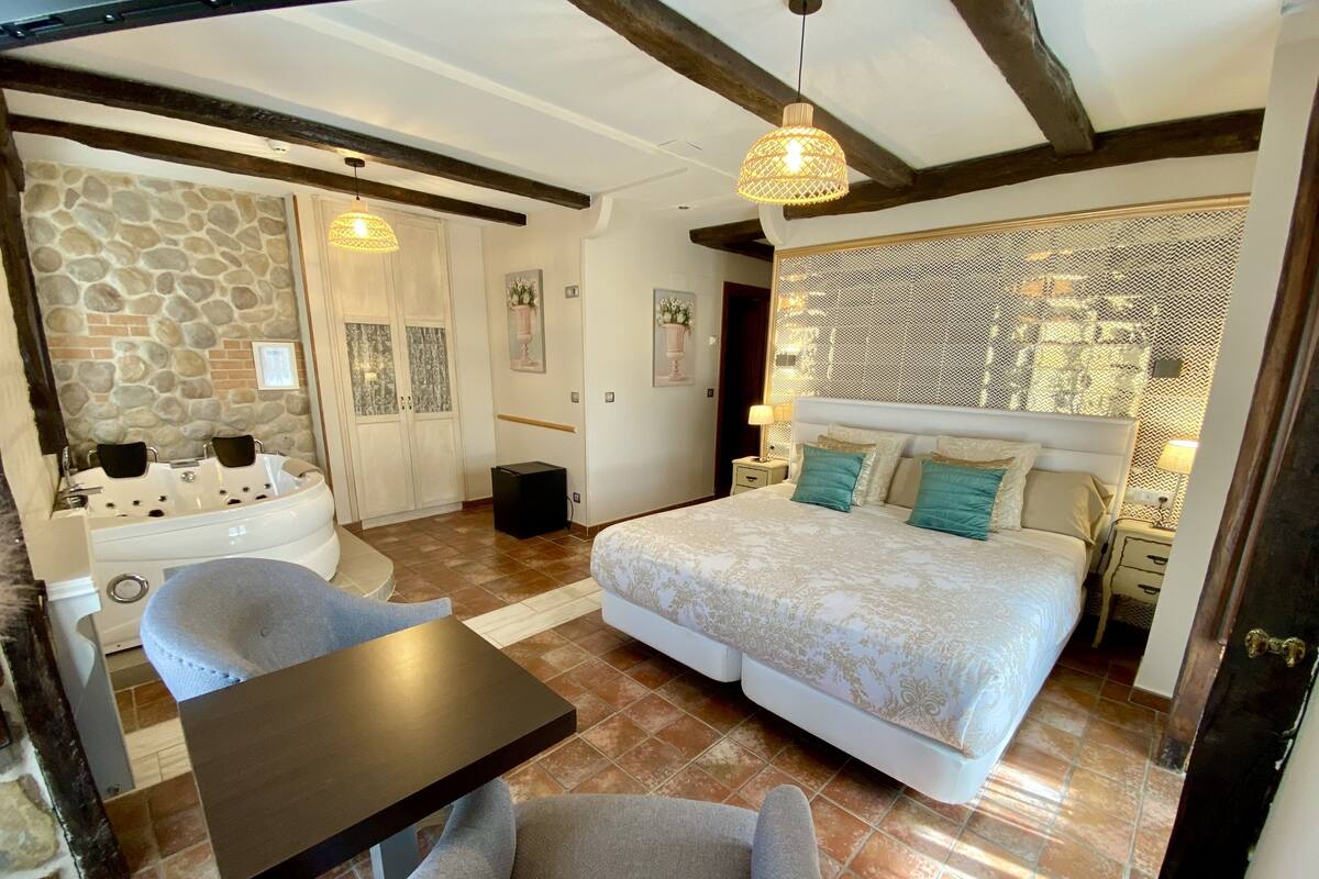Ein Schlafzimmer mit Bett, Stuhl, Tisch, einer Steinwand und einer Holzbalkendecke.